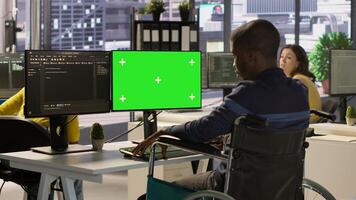 Person with disability testing and deploying programs and systems on green screen PC. Software technician in wheelchair checking code on mockup PC, sitting at desk in office, camera A photo