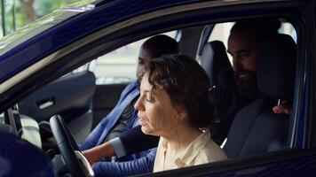 Salesman discussing with clients doing test drive before buying car, talking about safety features. Couple purchasing new vehicle, evaluating how it feels, camera B close up photo