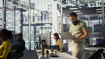 Admin at office desk utilizing cloud computing resources on laptop to train large scale machine learning models. Man monitoring company systems using notebook while standing in workspace, camera B photo