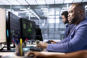 Teamworking technicians in data center getting access granted notification on PC screen, managing to access server files after they were locked by hacker using ransomware, receiving aid from coworkers photo