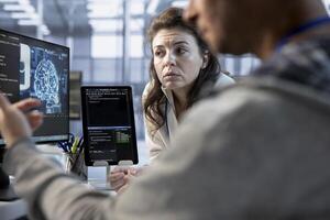 Engineer working with colleague on computer in artificial intelligence data center establishment monitoring hardware energy consumption. Team of AI technicians using PC to check for system failures photo
