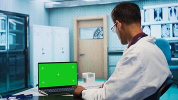 Indian physician works in his facility office next to chroma key, using modern technology for scan interpretation and results. Specialist offers professional advice based on records. Camera B. photo