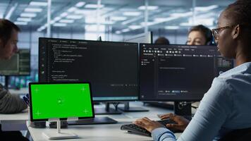 Isolated screen tablet in front of IT support workers coding on computers, upgrading equipment. Engineers at PC desk overseeing server clusters using chroma key device, camera B photo