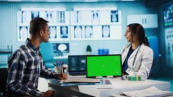 Indian physician consulting male patient in medical facility next to chroma key, using technology for scan interpretation and diagnostics. Medic giving professional advice based on records. Camera A. photo