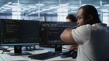 Ill Admin programming in server room housing advanced equipment coming up with flu, feeling sick. Developer suffering from cold, coughing while typing code on PC to mend data center racks, camera B photo