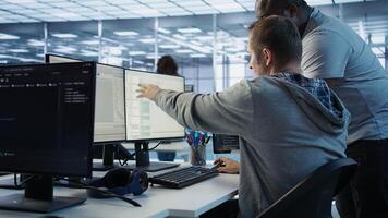 Programmer requesting help from manager while working on computer in data center, monitoring hardware energy consumption. Team leader overseeing IT expert checking for system failures, camera B photo