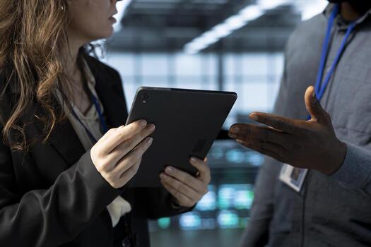 Teamworking employees in data center facility use tablet, configuring rigs network virtualization. IT professional and colleague in server farm updating storage arrays with device, verifying settings photo