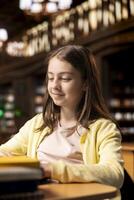 Young scholar takes notes for a descriptive essay work on laptop, completing an academic project in a school library. Student girl uses internet resources for a class assignment. Knowledge. photo