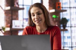 Ambitious woman learning a new language alone at her home office, browsing the internet for study platforms and explanations. Adult using a language learning software online on her laptop. photo