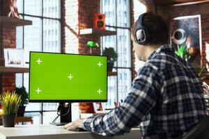 Worker wearing headphones engaging in online training session on chroma key PC, navigating course modules. Employee watching instructional company videos on mockup computer photo