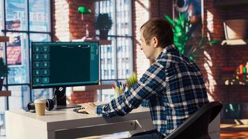 Man seated at desk using AI LLM chatbot software in modern urban home office. Person requesting help from large language model program on computer in bright apartment workspace, camera B photo