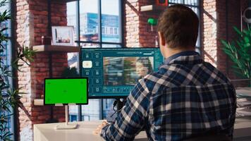 Man in home office uses AI program turning text prompt into videos next to isolated screen tablet. Person using text to generative models on computer and chroma key device, camera A photo