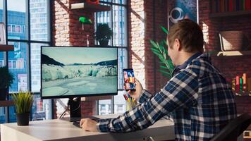 Man at home having fun looking at social media reels done by online content creators. Employee taking break from work to use mobile social network app, screensaver activating on PC, camera A photo