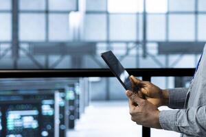 Engineer in data center using tablet, integrating green technologies, close up shot. Server room technician implementing sustainable energy solutions to maintain environmental standards photo
