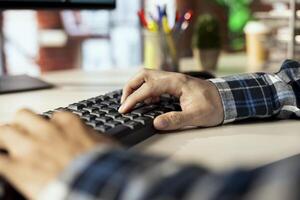 Close up shot of man at home office desk using computer, typing on keyboard, editing documents. Employee at workstation in workspace using PC to complete spreadsheets, solving tasks photo
