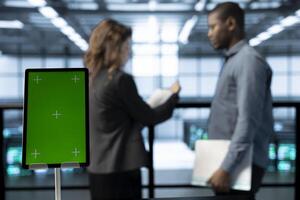 Focus on mockup device in front of data center technicians in blurry background analyzing metrics. Close up of green screen tablet next to server hub workers ensuring seamless operations photo
