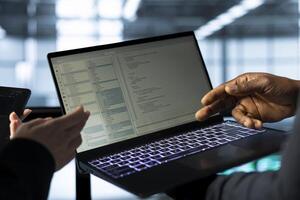 Software developers in data center using laptop, analyzing metrics, optimizing storage volumes. IT specialists in server hub facility using notebook, discussing, ensuring seamless operations photo