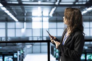 Programmer in data center facility uses tablet, configuring rigs network virtualization. IT expert in server farm updating storage arrays with device, verifying settings to maintain stable performance photo