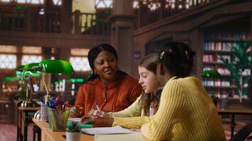 Black teacher mentoring her teen girls students with an assignment, teaching academic concepts and enhancing their knowledge through practical exercises. Private lessons at the library. Camera B. photo
