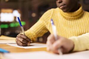 Diverse preteens writing class notes in their notebooks at a library desk, preparing for an academic assessment after classes. Literary ideas on paper, emphasizing child development. Close up. photo