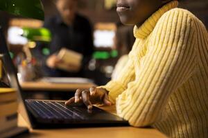 African american schoolgirl writing class notes at a study desk in a library, working hard on a school project with online information on laptop. Pupil preparing for lessons at the academic institute. photo
