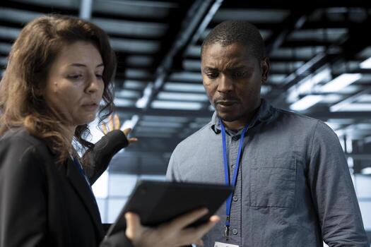 Team of engineers in data center talking, using tablet to do network virtualization. Coworkers doing brainstorming in server farm, updating storage arrays with device, verifying settings photo