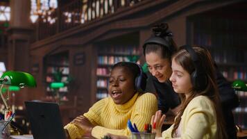 Young students and tutor attending an online class via call in the library, focused on distance learning and completing a school assignment with other classmates on the network. Camera B. photo