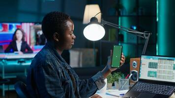 Teleworker in home office checks statistics on laptop, crosschecking with data on green screen smartphone. Person holding mockup mobile phone, analyzing company revenue numbers photo