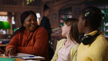 Diverse teen girls working with a tutor to complete class notes in a library, helps with learning and tutoring for the school subjects. Professor ensures diversity and child development. Camera B. photo