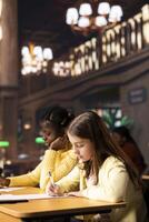 Diverse schoolgirls taking notes and completing theoretical exercises in a public library, showcasing positive academic development and a productive homework session. Scholars solve assignments. photo