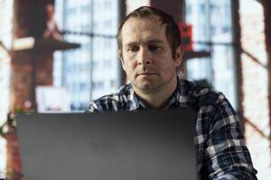 Man at home office desk using laptop, preparing presentation slides, inserting charts, adjusting layouts, writing summaries, saving files, uploading presentation materials to shared drive photo