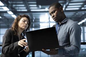 Team of engineers working in server farm, using laptops to analyze data. Teamworking employees examining infrastructure in data center, ensuring system integrity and security photo