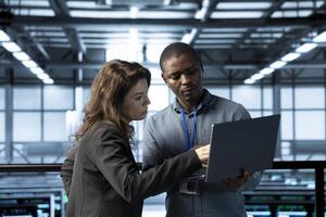 Computer scientists in data center using notebook, integrating green technologies. African american man and colleague in server room implementing sustainable energy solutions photo