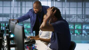 Server room engineers panicking after seeing disaster recovery plans fail, unable to avoid downtime. Stressed data center workers frightened after seeing performance drop while monitoring it, camera A photo