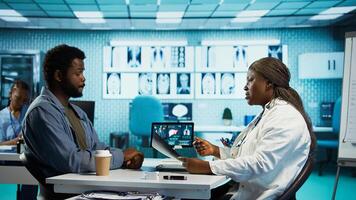 General practitioner reviewing x ray imaging at checkup with male patient, offering her professional expertise to ensure wellness. Medic doing scan interpretation with a man in the office. Camera B. photo