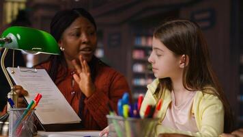 African american professor mentoring diverse schoolgirls in the library, learning together in a library filled with curriculum based materials. Woman tutoring pupils on literature. Camera B. photo