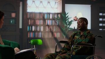 Black army soldier in wheelchair is a war survivor and deals with shell shock, experiencing a bad case of PTSD and anxiety. Wounded trooper opening up about horror combat scenes. Camera A. photo