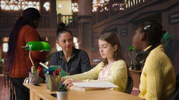 Female tutor mentoring schoolgirls in a school library setting, boosting their understanding of a subject through personalized guidance. Teacher doing private lessons with two pupils. Camera A. photo