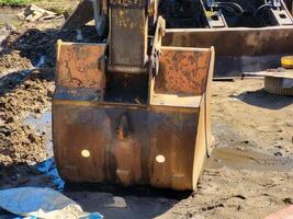 A bucket of an idle excavator is lying on the wet ground. photo