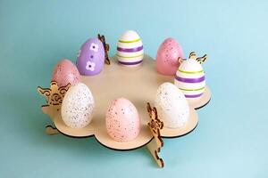 Multicolored eggs the color of Peach Fuzz speckled, stand on a wooden stand on a blue background. The concept of the Easter holiday. photo