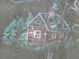 Drawing in multicolored chalk of a house with Christmas trees on the asphalt. photo