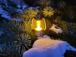A small decorative lantern stands in the snow on the branches of a fir tree. The concept of New Year and Christmas photo