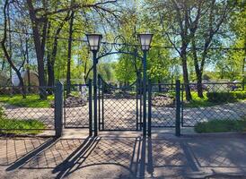 On a sunny spring day, a wrought-iron fence, a gate and lanterns in a small town park photo