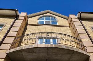 Beautiful yellow facade of a two-storey house with a wrought-iron balcony and large windows photo
