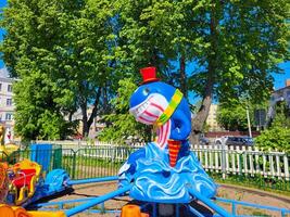 In the sunny spring park, there is a Children's carousel with a blue cheerful whale in a red top hat. photo