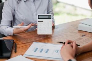 Professionals discussing financial data with a calculator and charts on a wooden table during a business meeting. photo