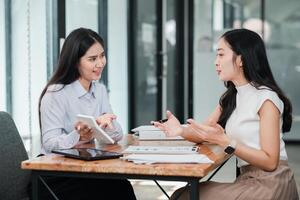 Two women having a business meeting in a modern office setting, discussing work with digital tablets and documents on the table. photo