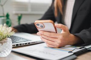 Close-up of a business professional using a smartphone and laptop at a desk, showcasing modern work and communication. photo