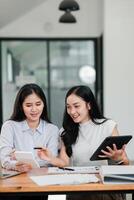 Two women working together in a modern office, using digital devices and discussing documents. photo