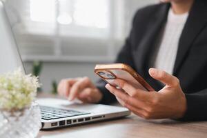 Professional working on a laptop while checking a smartphone in a bright, modern office environment. photo